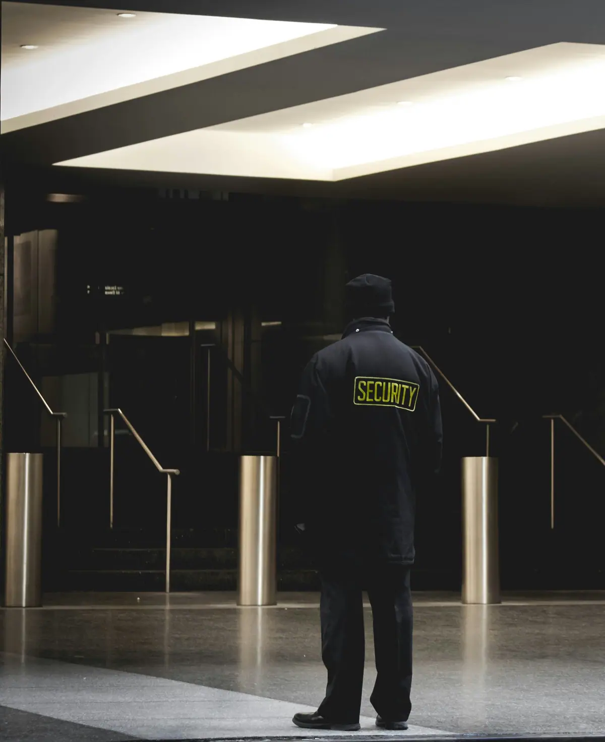 A security officer seen from behind, watching the turnstiles of an office lobby at night.