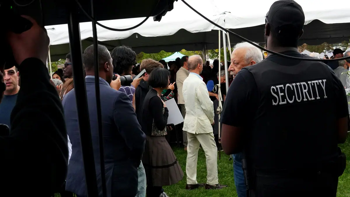 A security officer watching over a crowd gathered under a tent at an outdoor event.