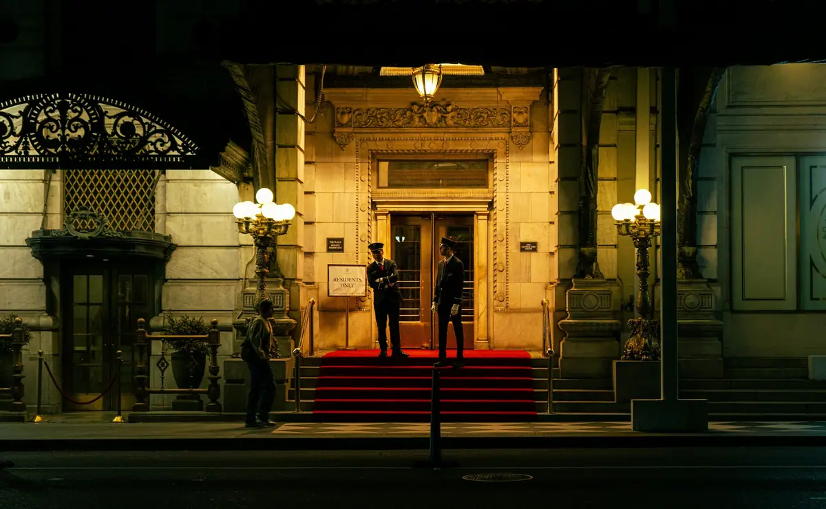 Two uniformed staff at the lit entrance of a grand building at night.